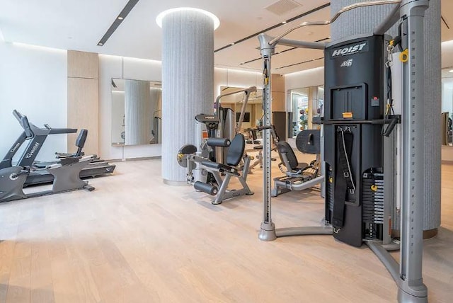 exercise room with ornate columns and light wood-type flooring