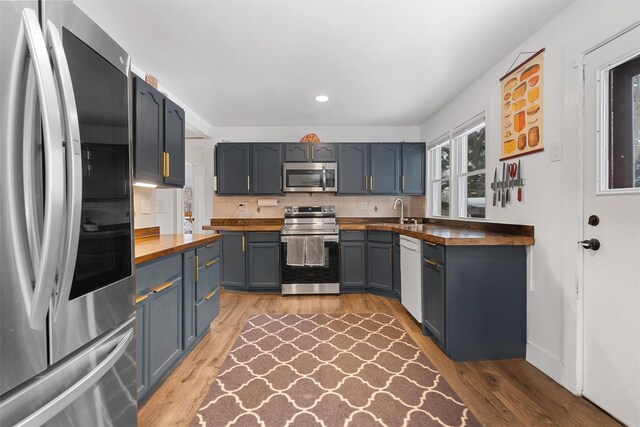 kitchen featuring butcher block countertops, hardwood / wood-style flooring, sink, appliances with stainless steel finishes, and tasteful backsplash