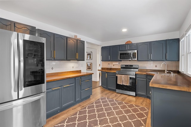 kitchen with sink, light hardwood / wood-style flooring, appliances with stainless steel finishes, tasteful backsplash, and wood counters