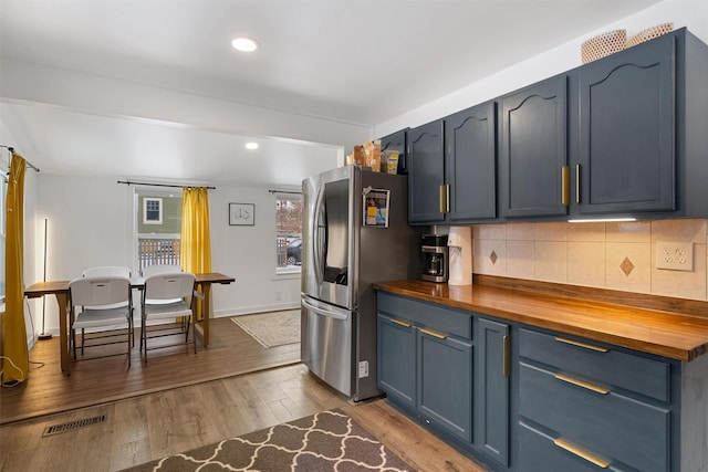 kitchen featuring butcher block countertops, blue cabinets, backsplash, stainless steel fridge, and light hardwood / wood-style flooring