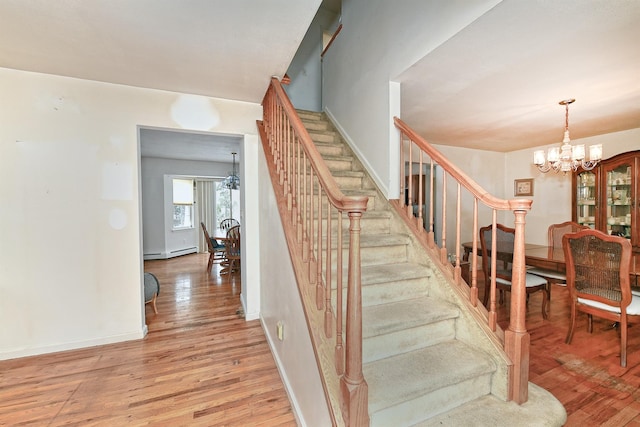 stairway with baseboard heating, hardwood / wood-style floors, and a notable chandelier