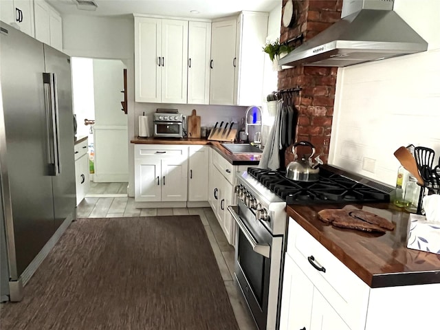 kitchen featuring high end appliances, wall chimney range hood, white cabinetry, and sink