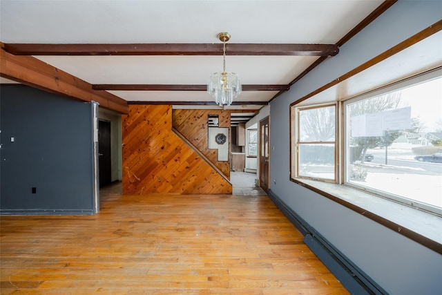 unfurnished living room with beam ceiling, wooden walls, light hardwood / wood-style floors, and a chandelier