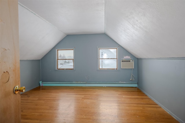 bonus room with light hardwood / wood-style flooring, an AC wall unit, a textured ceiling, and vaulted ceiling