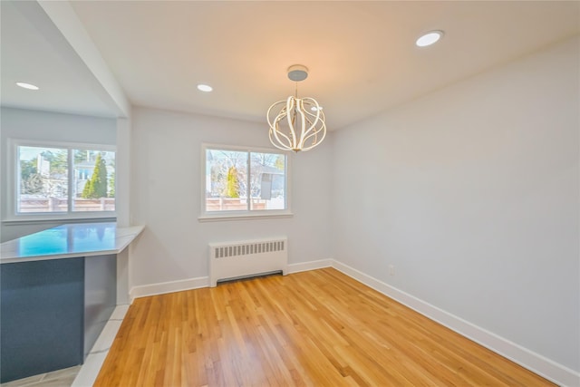 unfurnished dining area with radiator, plenty of natural light, light hardwood / wood-style floors, and a chandelier