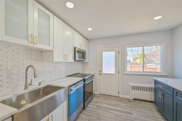 kitchen featuring sink, white cabinetry, light stone counters, radiator, and stainless steel appliances