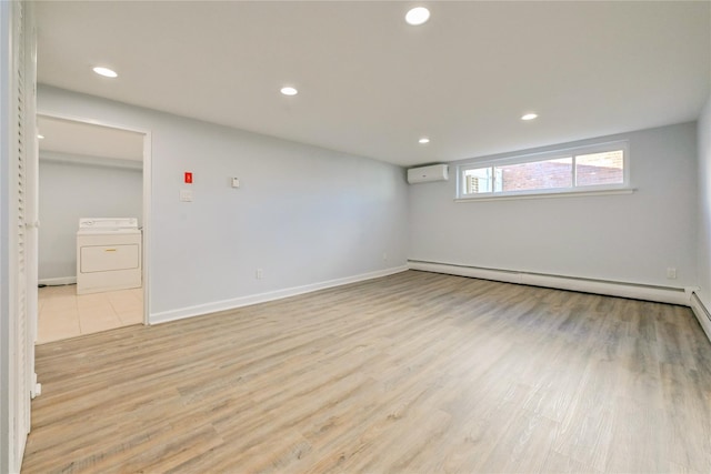 spare room with washer / dryer, a baseboard heating unit, a wall unit AC, and light hardwood / wood-style floors