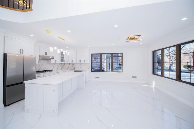 kitchen with appliances with stainless steel finishes, white cabinetry, a center island, ornamental molding, and decorative light fixtures