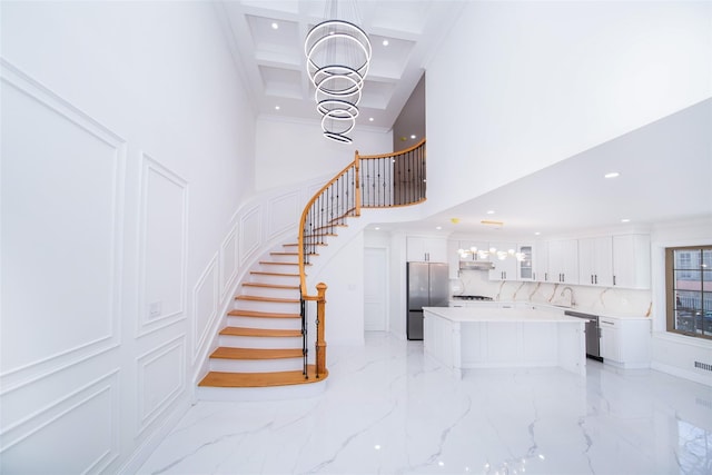 stairs with a towering ceiling, sink, coffered ceiling, crown molding, and beam ceiling