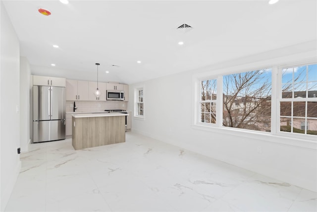 kitchen with lofted ceiling, appliances with stainless steel finishes, a center island, tasteful backsplash, and decorative light fixtures