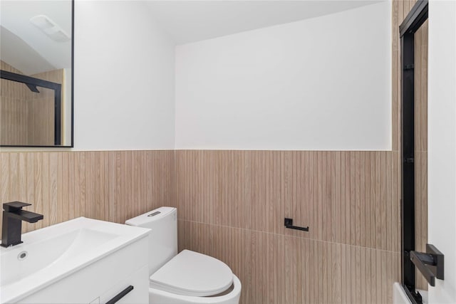 bathroom featuring vaulted ceiling, a shower with shower door, tile walls, vanity, and toilet