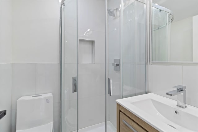 bathroom with vanity, a shower with door, tile walls, and toilet