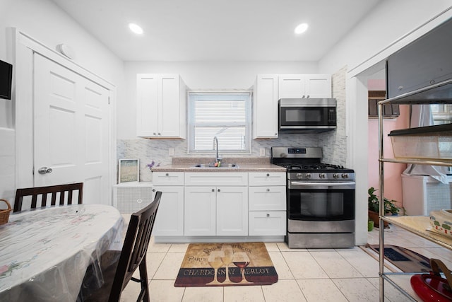 kitchen with sink, light tile patterned floors, white cabinetry, stainless steel appliances, and light stone counters