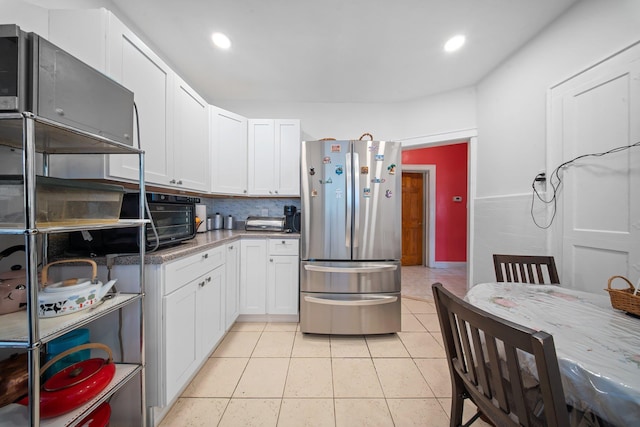 kitchen with stainless steel fridge, white cabinetry, backsplash, light stone counters, and light tile patterned flooring