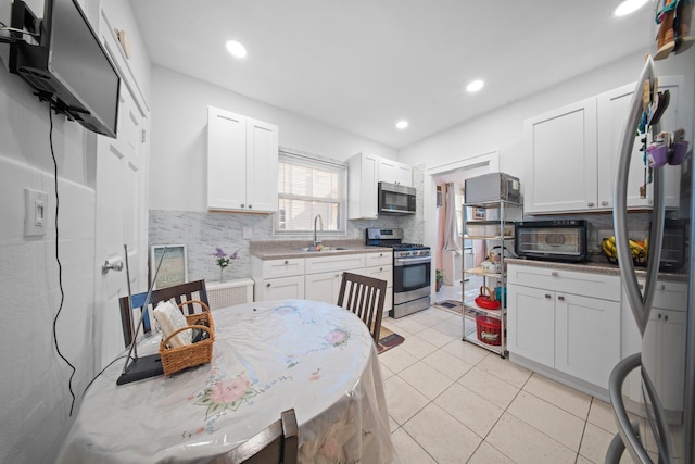 kitchen featuring light tile patterned flooring, appliances with stainless steel finishes, white cabinetry, sink, and backsplash