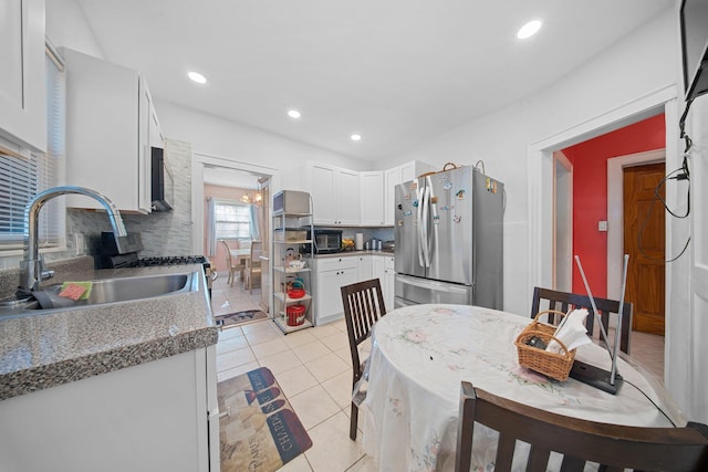 kitchen with sink, stainless steel fridge, white cabinets, light stone countertops, and backsplash