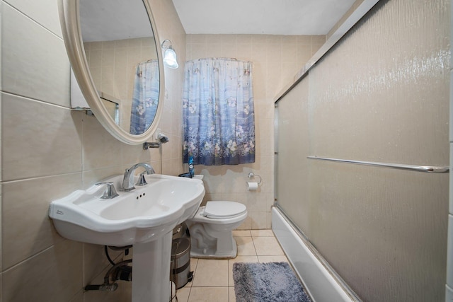 bathroom featuring toilet, tile patterned floors, shower / bath combination with glass door, and tile walls