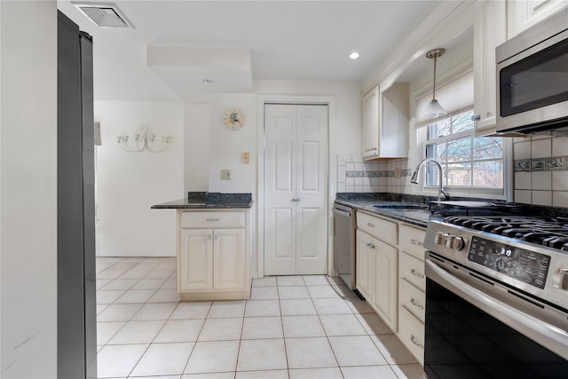 kitchen with sink, decorative light fixtures, light tile patterned floors, dark stone countertops, and stainless steel appliances