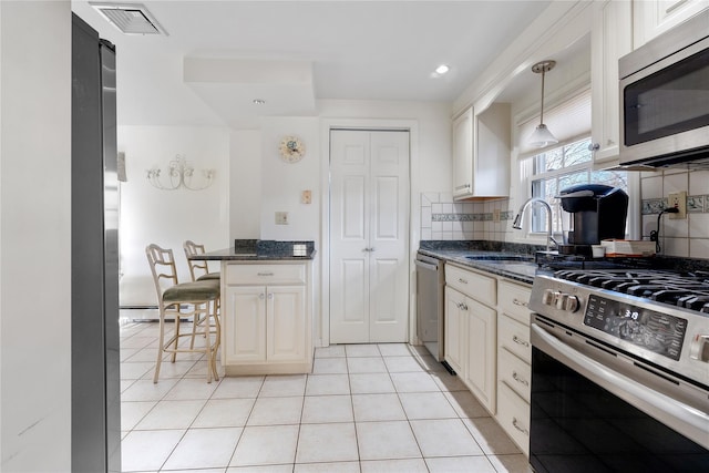 kitchen with appliances with stainless steel finishes, decorative light fixtures, sink, dark stone countertops, and a kitchen breakfast bar