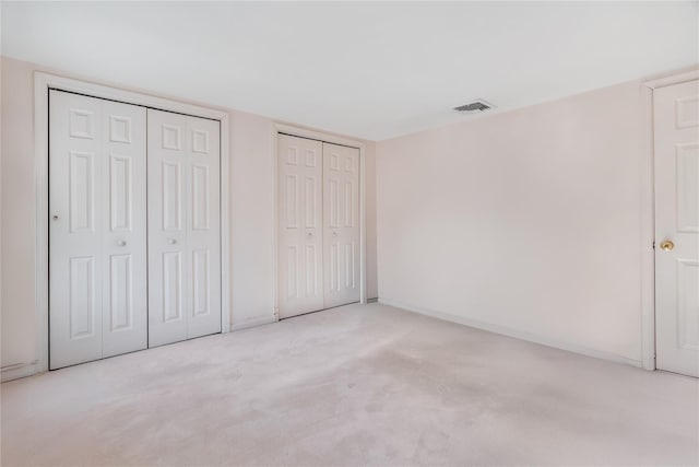 unfurnished bedroom with light carpet and two closets