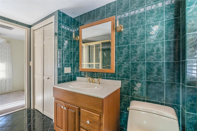 bathroom with tile walls, tile patterned flooring, vanity, toilet, and walk in shower