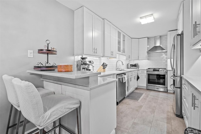 kitchen with white cabinetry, wall chimney range hood, a breakfast bar, and appliances with stainless steel finishes