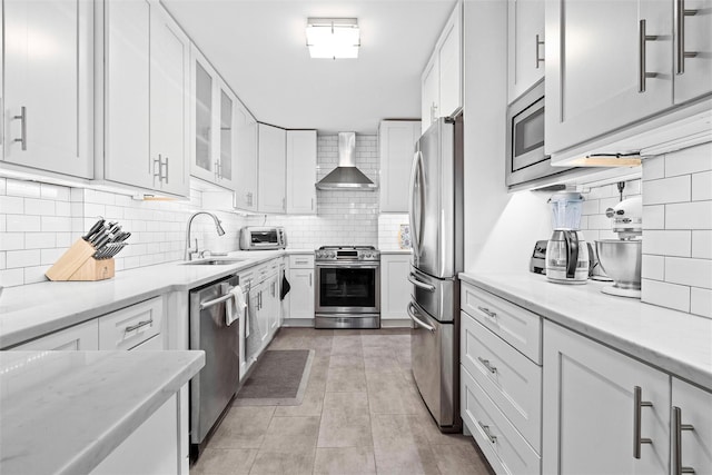 kitchen featuring sink, appliances with stainless steel finishes, light stone counters, white cabinets, and wall chimney exhaust hood