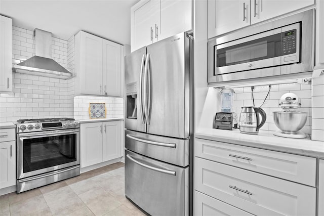 kitchen with white cabinets, decorative backsplash, wall chimney exhaust hood, and appliances with stainless steel finishes