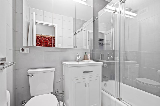 full bathroom featuring toilet, tasteful backsplash, bath / shower combo with glass door, tile walls, and vanity