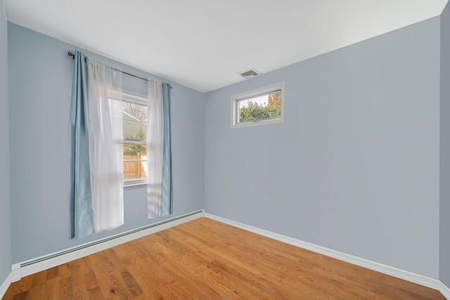 unfurnished room featuring hardwood / wood-style flooring, a healthy amount of sunlight, and baseboard heating