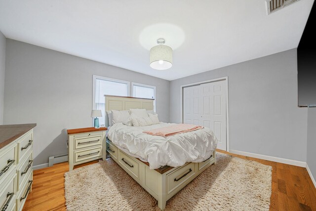 bedroom with a baseboard radiator, light hardwood / wood-style floors, and a closet