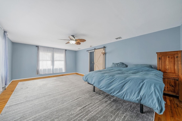 bedroom with hardwood / wood-style floors, a barn door, and ceiling fan