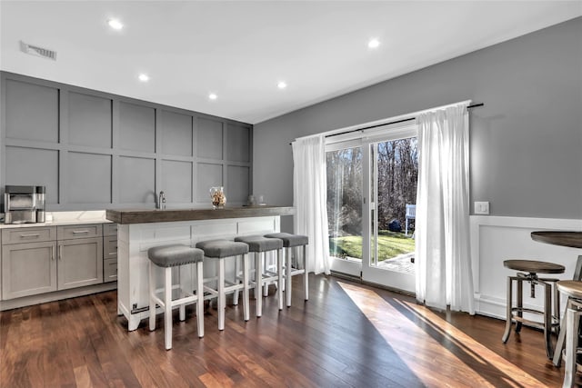 kitchen with dark wood-type flooring, gray cabinets, sink, and a breakfast bar area