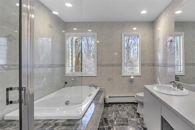 bathroom with a relaxing tiled tub, vanity, tile walls, and a baseboard heating unit