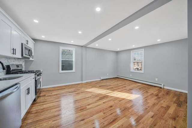 kitchen featuring sink, appliances with stainless steel finishes, white cabinetry, a baseboard heating unit, and light hardwood / wood-style floors