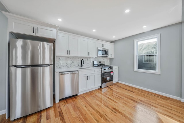 kitchen with sink, backsplash, white cabinets, and appliances with stainless steel finishes