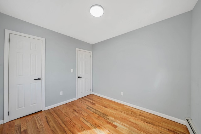 unfurnished room with wood-type flooring and a baseboard heating unit