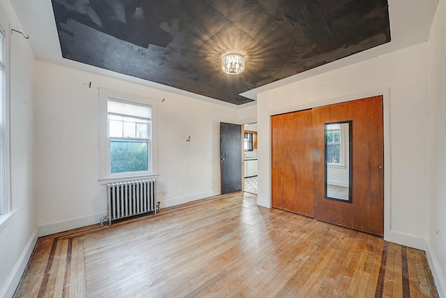 unfurnished bedroom featuring radiator, light hardwood / wood-style floors, and a closet