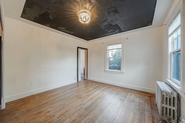 unfurnished room with a tray ceiling, radiator, and hardwood / wood-style floors