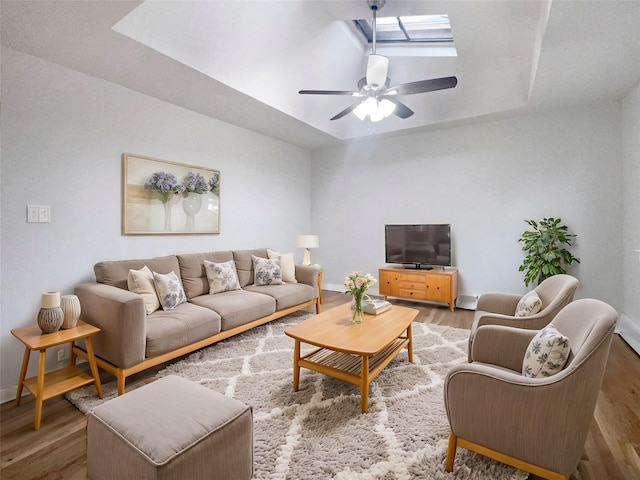 living room featuring a skylight, wood-type flooring, a raised ceiling, and ceiling fan