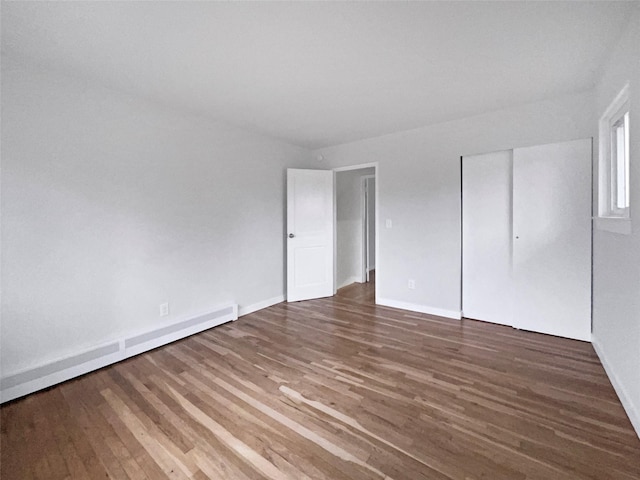 unfurnished bedroom featuring a baseboard heating unit, dark hardwood / wood-style floors, and a closet