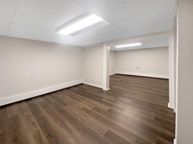 basement with a baseboard heating unit, a paneled ceiling, and dark hardwood / wood-style flooring