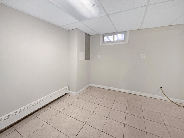 basement with baseboard heating, a paneled ceiling, and light tile patterned flooring