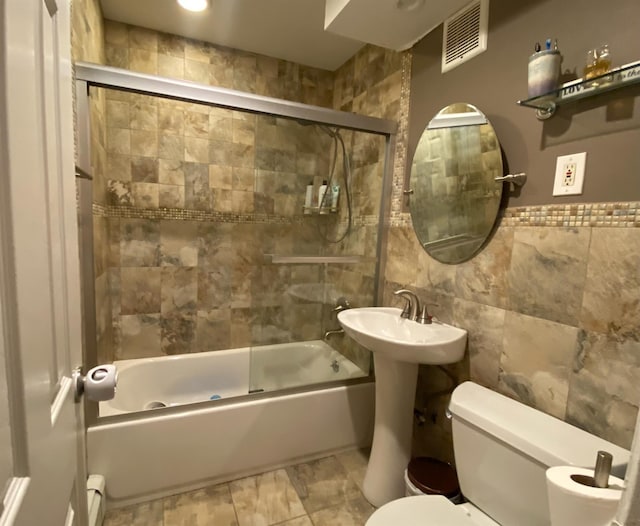 bathroom featuring visible vents, shower / bath combination with glass door, tile walls, and toilet