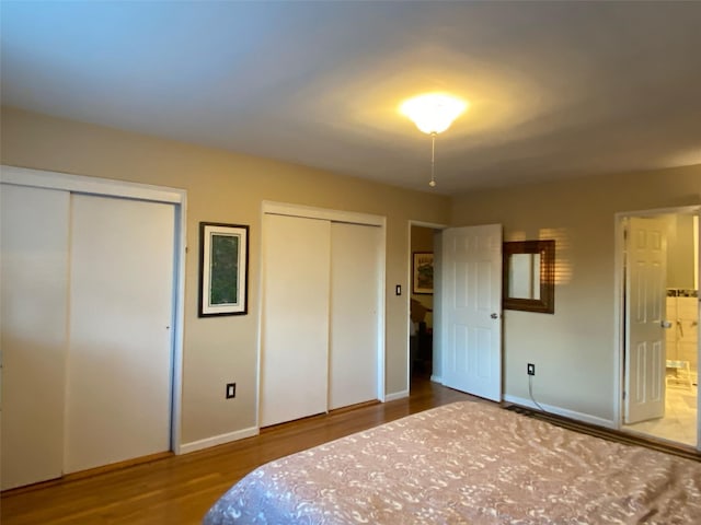 unfurnished bedroom featuring multiple closets, connected bathroom, baseboards, and wood finished floors