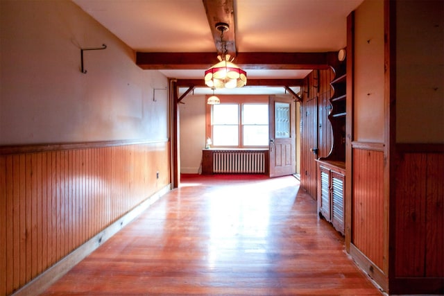 hall featuring beamed ceiling, wooden walls, radiator, and light hardwood / wood-style floors