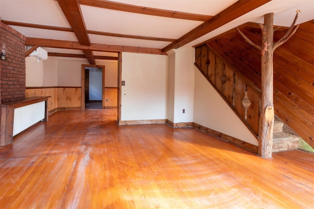 unfurnished living room featuring hardwood / wood-style flooring, radiator heating unit, an AC wall unit, beamed ceiling, and wood walls