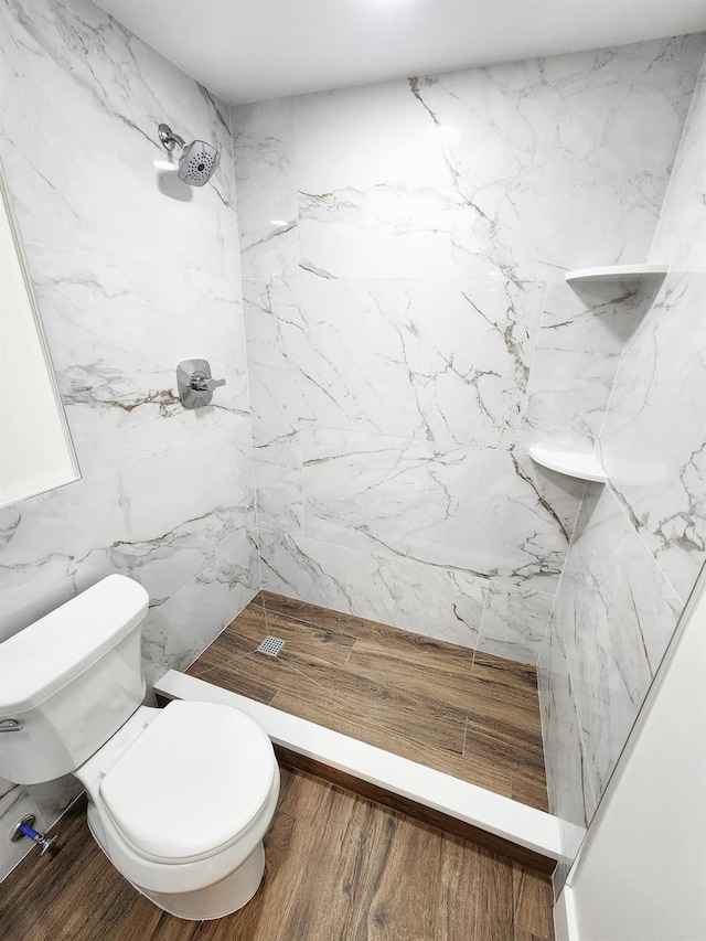 bathroom with wood-type flooring, toilet, and a tile shower