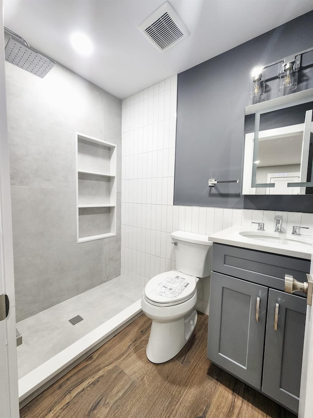 bathroom with hardwood / wood-style flooring, toilet, tile walls, and a tile shower