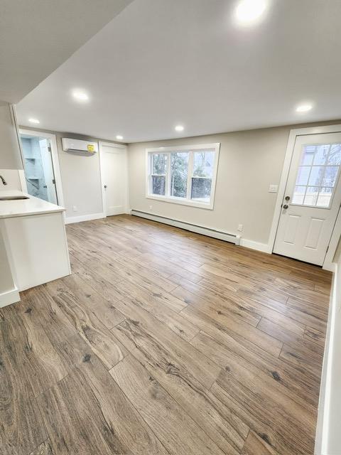 unfurnished living room with a baseboard radiator, sink, a wall mounted air conditioner, and light hardwood / wood-style floors